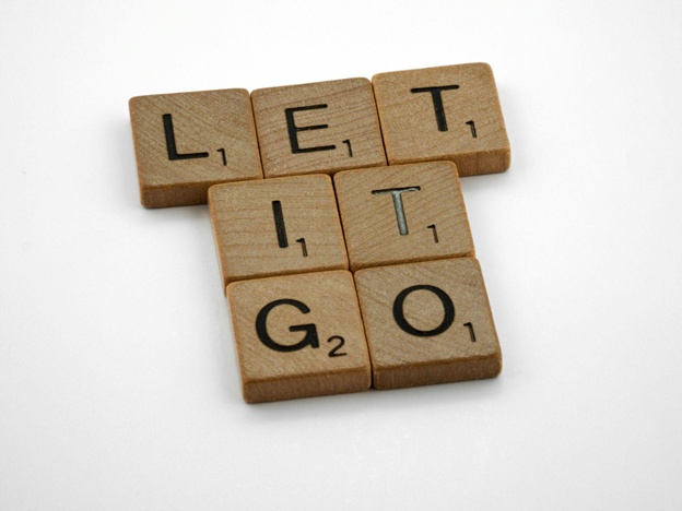 Scrabble tiles on a white surface spell "LET IT GO" vertically and horizontally.